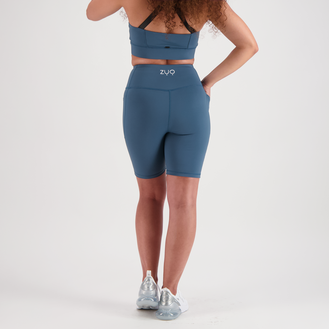 Back view, model in mid-length shorts in Arctic Teal, a dusty blue-green colour